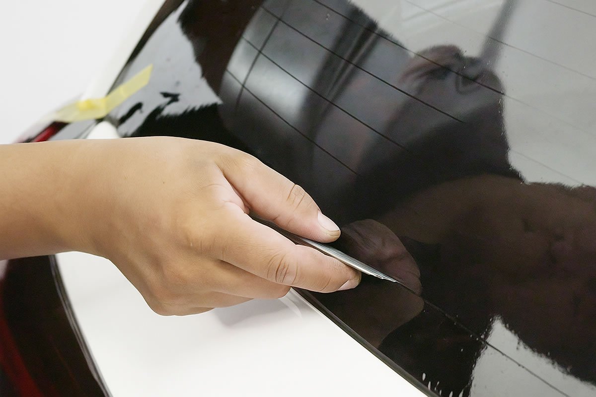 Corte preciso de lámina polarizada con bisturí NT Cutter sobre vidrio lateral de automóvil.