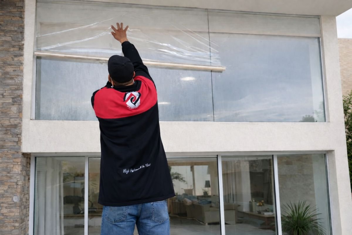 Técnico instalando película de seguridad arquitectónica en ventanal de edificio moderno para reforzar protección y resistencia del vidrio.